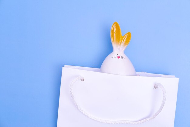 Shopping per la Pasqua Borsa della spesa in carta bianca con coniglietto bianco su sfondo blu Concetto Sorpresa dei regali di Pasqua