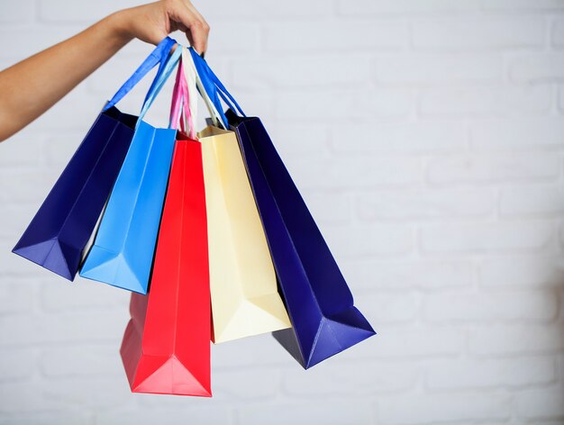 Shopping. Primo piano del sacchetto della spesa della carta di colore della tenuta della donna sul fondo bianco della parete