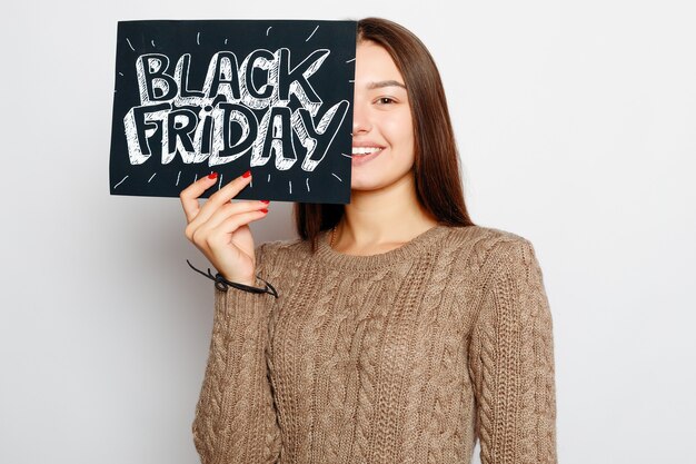 Shopping, vendita al dettaglio, venerdì nero, vendita, shopping e concetto di persone - giovane ragazza bruna sorridente sta tenendo un segno di venerdì nero