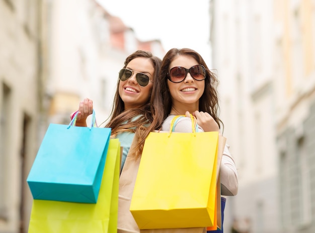 shopping, vendita, persone felici e concetto di turismo - due ragazze sorridenti in occhiali da sole con borse della spesa in ctiy