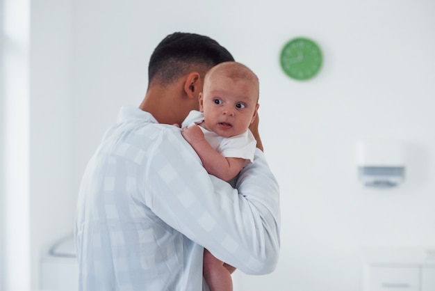 Si alza e tiene il bambino sulle mani. Il giovane pediatra è in clinica durante il giorno.