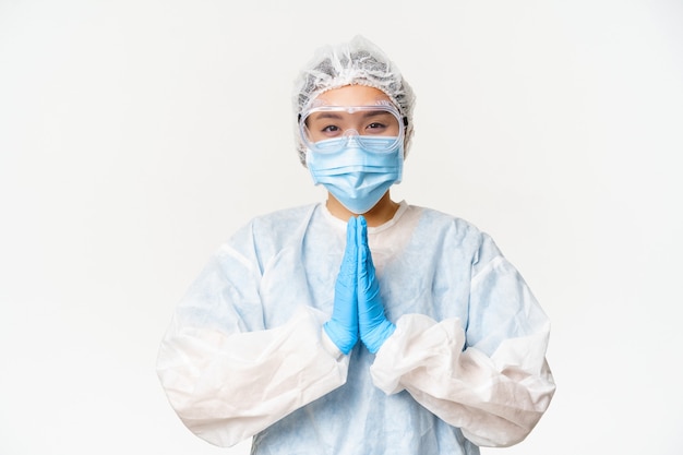 Si prega di vaccinare. Sorridente dottoressa asiatica o infermiere in dispositivi di protezione individuale, mostrando mendicante, chiedendo gesto, in piedi su sfondo bianco.