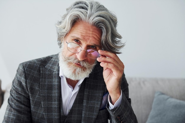 Si siede su un comodo divano in abiti formali Uomo moderno ed elegante con capelli grigi e barba all'interno