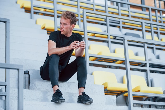 Si siede sulle scale Giovane sportivo in camicia nera e pantaloni all'aperto durante il giorno