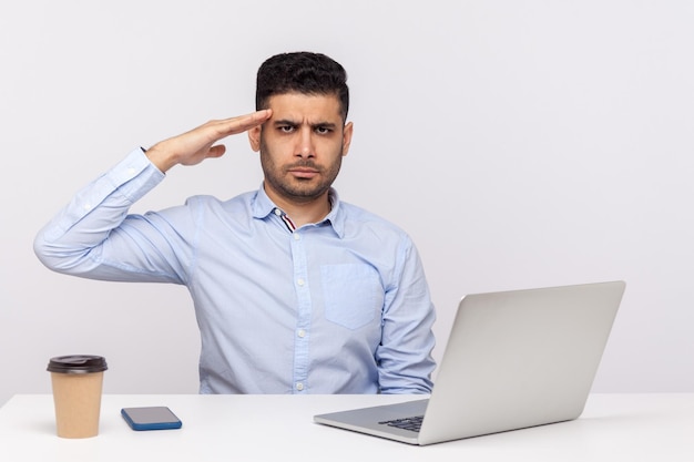 Si signore. Dipendente uomo responsabile seduto sul posto di lavoro dell'ufficio con il laptop sulla scrivania, guardando la fotocamera con saluto e pronto a fare il tuo ordine, seguendo la disciplina. girato in studio isolato su sfondo bianco