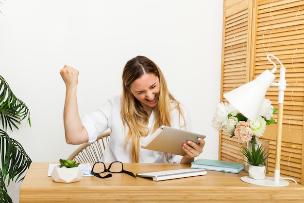 Sì. Stazione di lavoro emozionante felice della donna a casa che trionfa con le mani sollevate