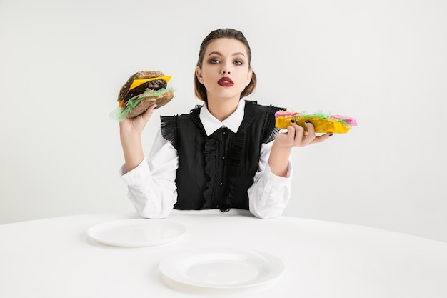 Siamo quello che mangiamo. La donna mangia hamburger e hot-dog di plastica, concetto di eco plastic