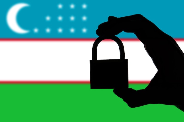 Sicurezza dell'Uzbekistan Silhouette di una mano che tiene un lucchetto sopra la bandiera nazionale