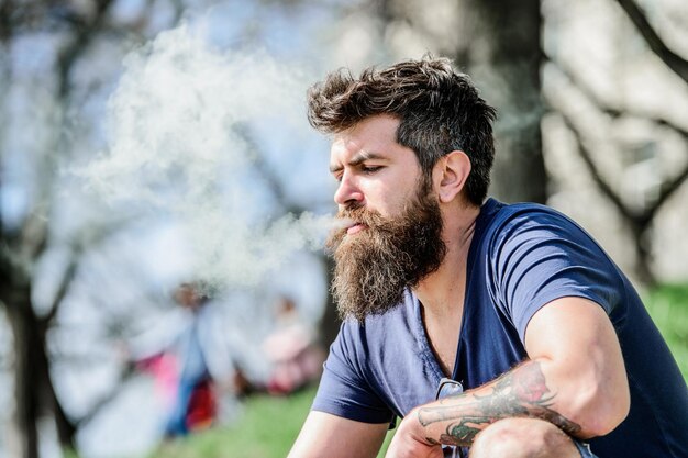 Sicurezza sanitaria e dipendenza inalando vapore uomo che fuma sigaretta hipster uomo tenere dispositivo di svapo Pantaloni a vita bassa maturi con barba Barbuto maschio brutale che fuma sigaretta elettronica Barbuto ed elegante