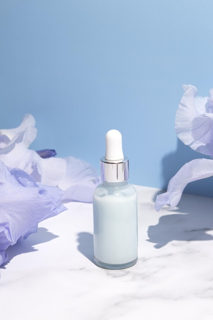 Siero con estratti floreali per la cura della pelle Cosmetici naturali in bottiglia di vetro con pipetta e fiori di iris su sfondo blu Concetto di spa per la cura del viso e del corpo