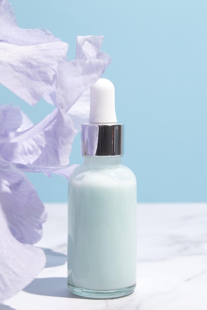 Siero con estratti floreali per la cura della pelle Cosmetici naturali in bottiglia di vetro con pipetta e fiori di iris su sfondo blu Concetto di spa per la cura del viso e del corpo