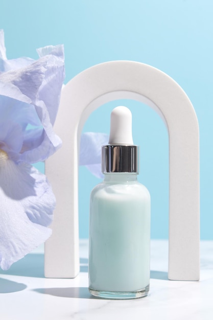 Siero con estratti floreali per la cura della pelle in arco Cosmetici naturali in bottiglia di vetro con pipetta e fiori di iris su sfondo blu Concetto di spa per la cura del viso e del corpo