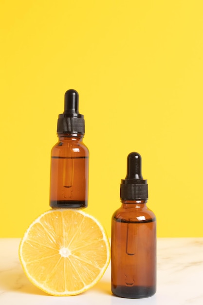 Siero con vitamina C Olio essenziale di limone Bottiglia di vetro con pipetta mezzo limone su sfondo giallo Concetto di salute e bellezza Cosmetici naturali biologici