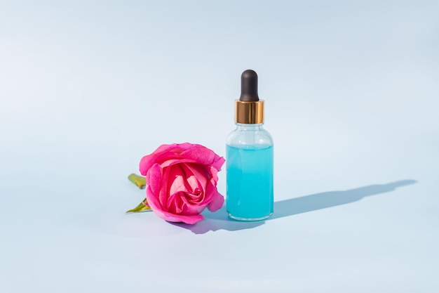 Siero cosmetico con olio essenziale di rosa e rose su fondo blu Un prodotto naturale per detossinare idratante tonificare e rigenerare la pelle Mockup di prodotto senza marchio