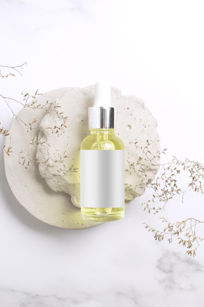 Siero cosmetico in bottiglia di vetro su podio di pietra Marchio di design del packaging di prodotti cosmetici naturali Sfondo in marmo con ramo di fiori