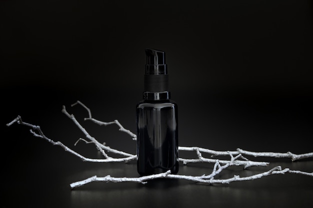 Siero cosmetico nero senza marchio con ramo d'albero d'argento. Presentazione del prodotto per la cura della pelle sullo sfondo nero. Modello elegante. Cura della pelle, bellezza e spa.