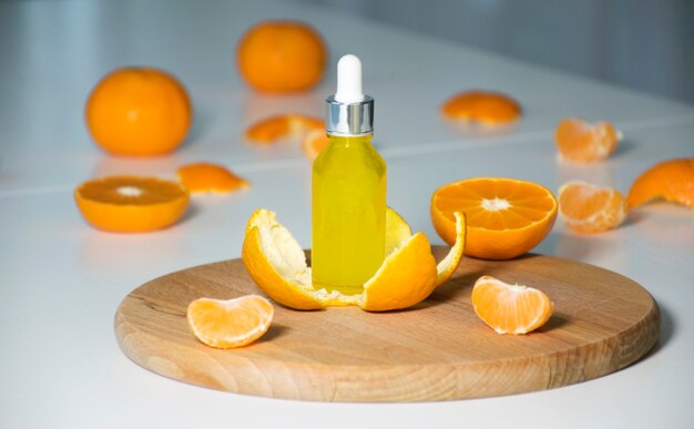 Siero di vitamina C in flacone cosmetico in scorza di mandarino con mandarini sullo sfondo. Olio essenziale di agrumi, cura della pelle del viso, cosmetici SPA biologici con ingredienti vegetali.