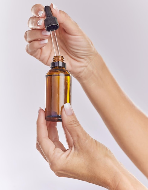 Siero per la cura della pelle olio essenziale e prodotto cosmetico nella mano della donna per una pelle liscia perfetta o per ridurre le rughe isolate sullo sfondo dello studio Mani del primo piano usando la cura del corpo o una goccia di liquido antietà