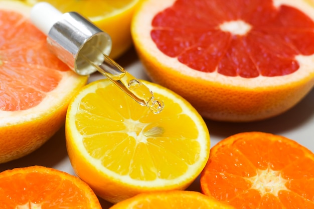 Siero viso con vitamina c con diversi agrumi su sfondo bianco.