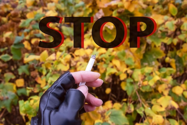 Sigaretta accesa in mano sullo sfondo di foglie gialle parola stop