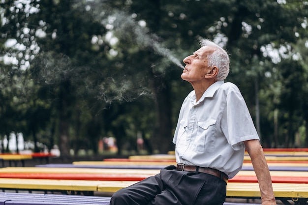 Sigaretta di fumo dell'uomo maggiore all'aperto nel parco della città