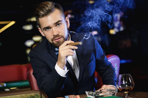 Sigaro di fumo dell'uomo bello ricco nel casinò