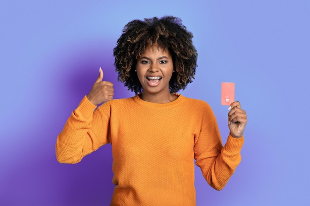 Signora afroamericana felice eccitata che mostra la carta di credito sulla porpora