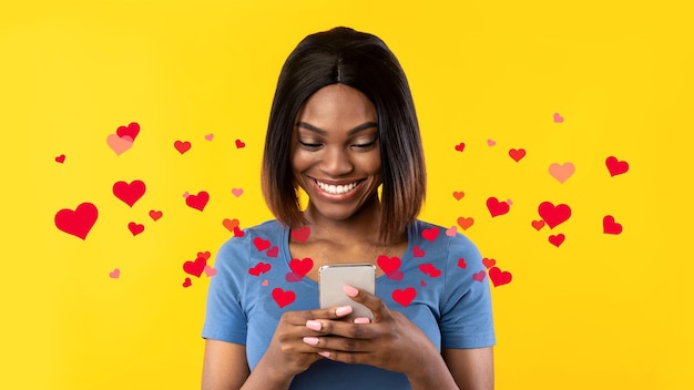 Signora afroamericana utilizzando il cellulare Texting su sfondo giallo studio