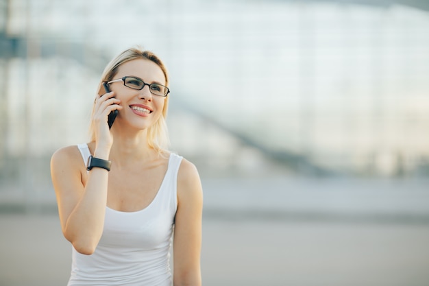 Signora alla moda di affari in vetri che parla sul telefono e sul sorridere