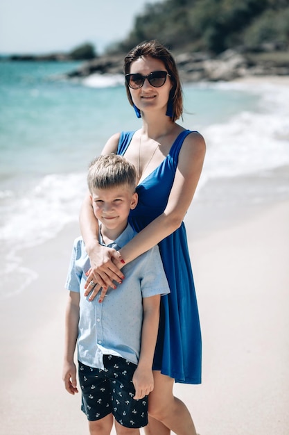 Signora alla moda in un vestito blu e figlio che posano per la macchina fotografica sulla spiaggia. Mamma che abbraccia suo figlio. Concetto di vacanza estiva al mare. Phuket. Tailandia. Vista sul mare blu.