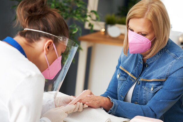 signora anziana che indossa una maschera nel salone di manicure