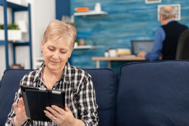 Signora anziana che si rilassa a casa sul divano leggendo un e-book