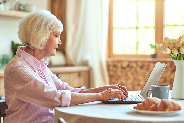 Signora anziana che usa un computer portatile a casa