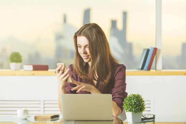 Signora attraente utilizzando il cellulare e il computer portatile