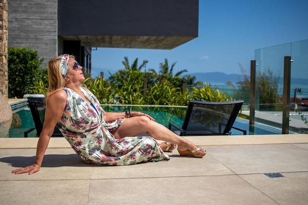 signora bionda in abiti da spiaggia e occhiali da sole seduti a bordo piscina in una giornata di sole e il cielo blu