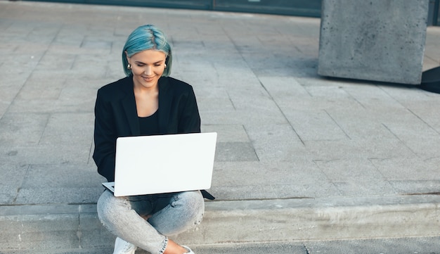 Signora caucasica con capelli blu che propone all'esterno con un computer mentre era seduto e lavorava