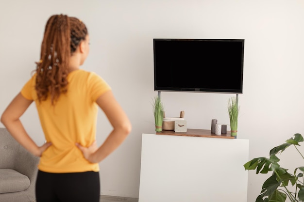 Signora che guarda lo schermo della tv che si esercita a casa vista posteriore