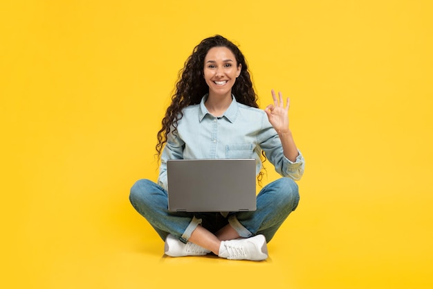 Signora che lavora al computer portatile che gesticola bene seduto su sfondo giallo