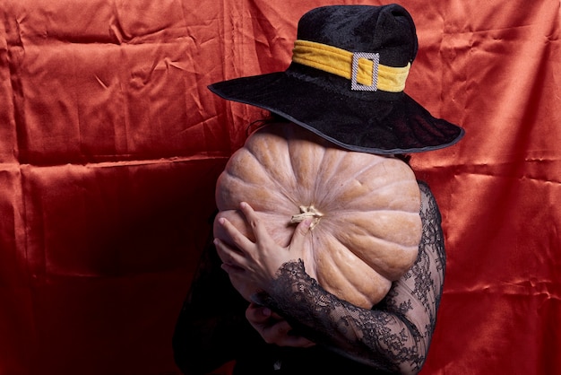 Signora di Halloween che indossa una tazza da strega e tiene in mano una grande zucca di Halloween una donna con un cappello da strega e un dono...