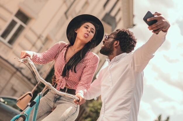 Signora divertente che mostra lingua e uomo sorridente che si fa selfie con lei