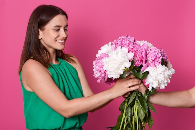 Signora e persona senza volto che dà il suo grande bellissimo mazzo di fiori, in posa isolato sul muro rosa