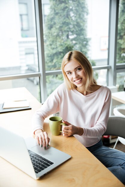 Signora felice che si siede nell'ufficio coworking mentre per mezzo del computer portatile