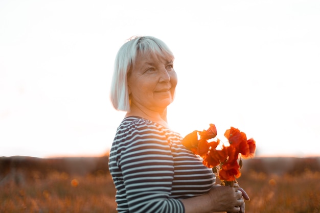 Signora felice della donna dei capelli biondi che tiene il mazzo dei papaveri rossi nel campo al tramonto