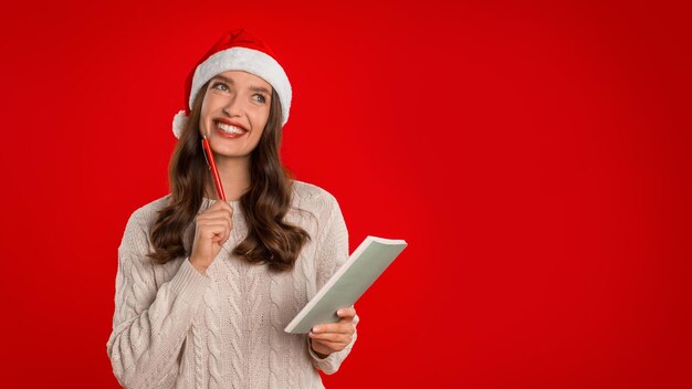 Signora felice in cappello di Babbo Natale in posa con sfondo rosso notebook