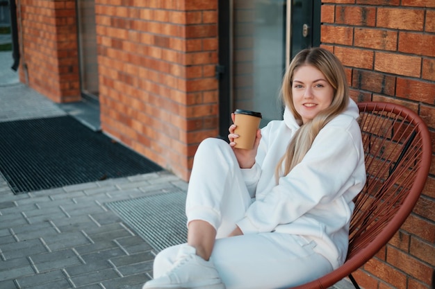 Signora in tuta sportiva bianca con caffè seduto all'aperto