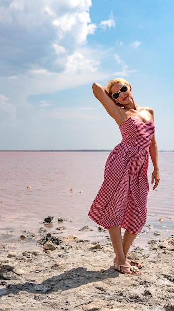 Signora in un bel vestito giovane con labbra tenere sullo sfondo di un lago rosso blu nuvole dentro