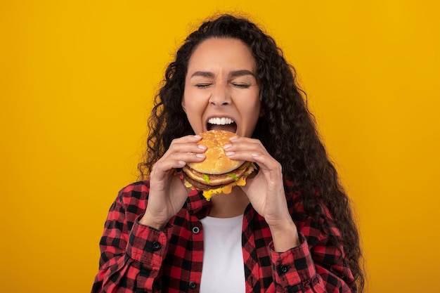 Signora latina divertente che tiene il panino mordace dell'hamburger allo studio