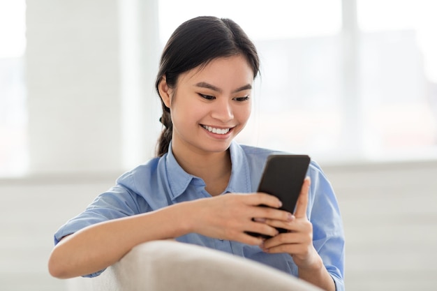 Signora sorridente che si siede sul sofà facendo uso del primo piano del telefono cellulare