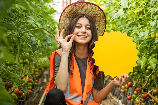 Signora sorridente che tiene il consiglio e il gesto dell'idea Ok alla serra