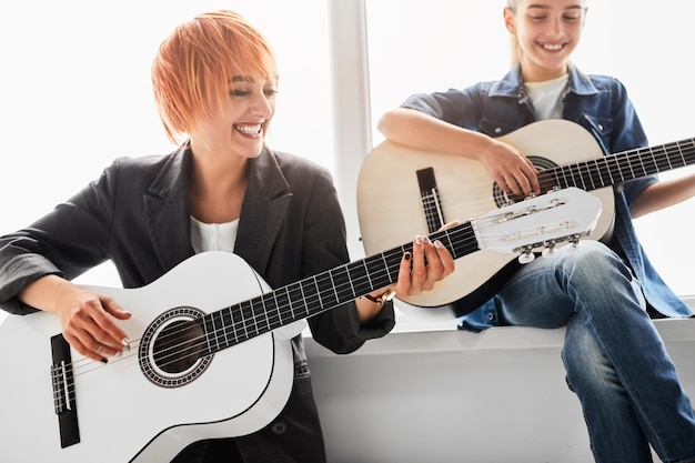 Signora sorridente con bambino che suona la chitarra vicino alla finestra in studio